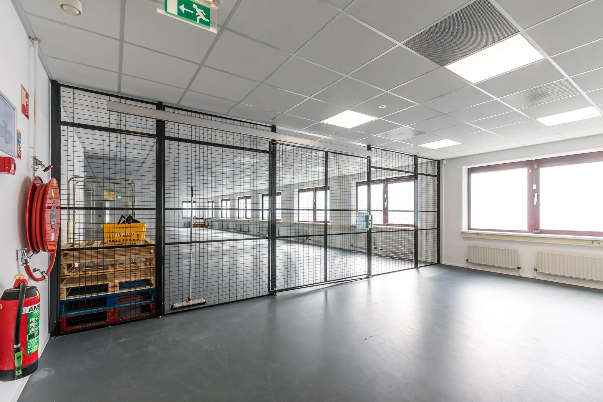 Industriële binnenruimte aan de Baarnsche Dijk met metalen hekwerk, palletopslag en brandslanghaspel.